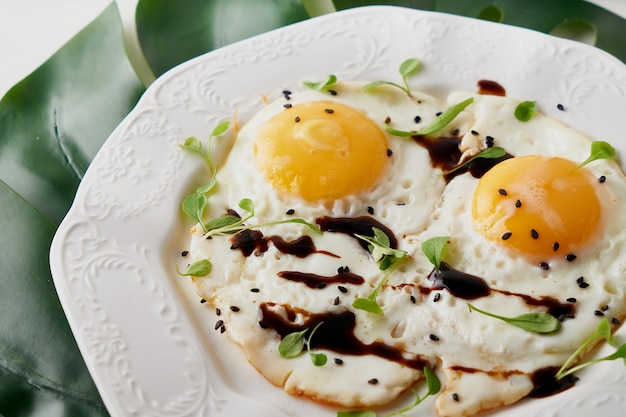 Morgenfrühstück mit Spiegeleiern und Pflanzenblatt auf weißem Tisch