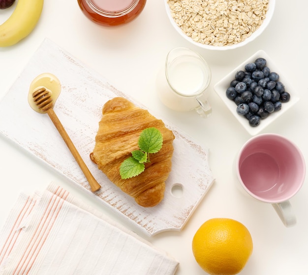 Morgenfrühstück rohe Haferflocken in einer Keramikplatte Milch in einem Dekanter Heidelbeeren und Honig in einem Glas auf einer weißen Tischplatte