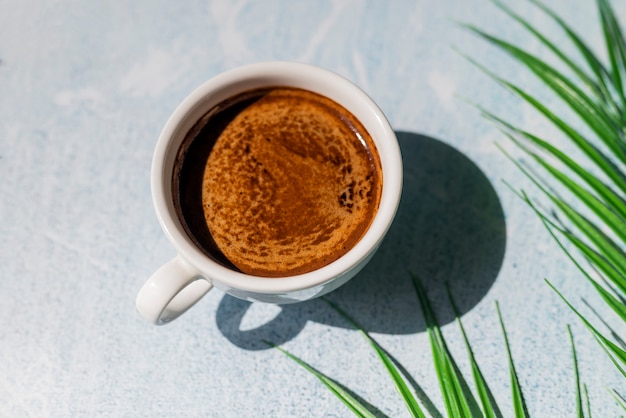 Morgenkaffee Americano in einer Tasse aromatischem Sonnenschein und Schatten mit einem Palmblatt