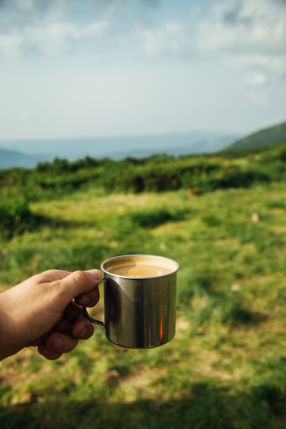 Morgenkaffee in einer eisernen Tasse in der Hand mit Blick auf ein Bergtal