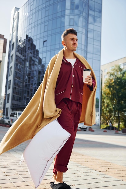 Morgenkaffeetasse Junger Mann im Pyjama ist draußen auf der Straße Fühlt sich schläfrig an