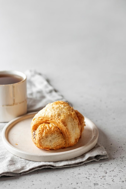 Morgenkonzept Frisches Croissant auf weißem Teller auf Serviette mit Tee auf hellem Hintergrund