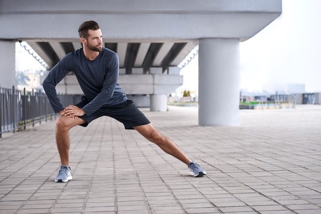 Morgens Aufwärmen vor dem Training gut aussehender junger Mann in Sportkleidung, der sich beim Aufwärmen ausdehnt