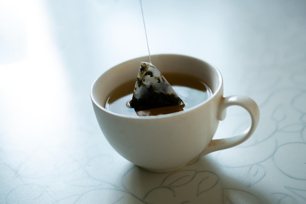 Morgens mit der Hand einen Pyramidenteebeutel in eine Tasse mit heißem Wasser geben