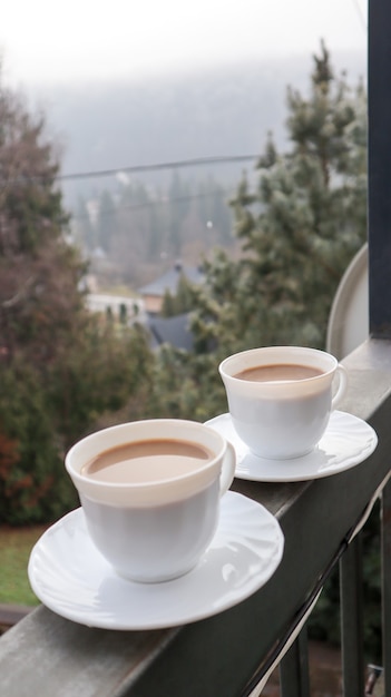 Morgens zwei Kaffeetassen auf einem Balkon mit Berglandschaft. Zwei Tassen Kaffee am Morgen, stehend auf der Seite des Balkons, mit einem zauberhaften Blick auf die herbstlichen Wälder.