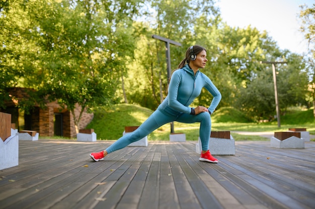 Morgentraining im Park, Frau in den Kopfhörern, die Fitnessübungen machen