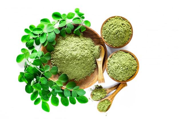 Moringa-pulver (moringa oleifera) in der hölzernen schüssel mit den ursprünglichen frischen moringa-blättern lokalisiert