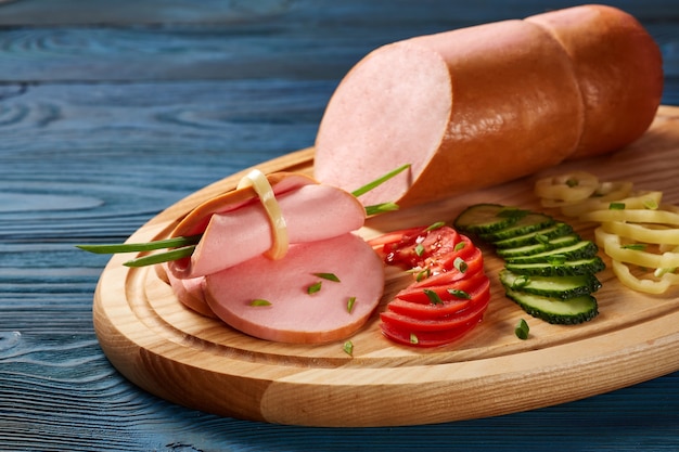 Mortadela con verduras y hierbas en una placa de madera sobre una mesa de madera.