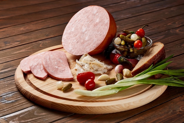 Foto mortadella mit gemüse und kräutern auf einem holzteller auf einem holztisch.