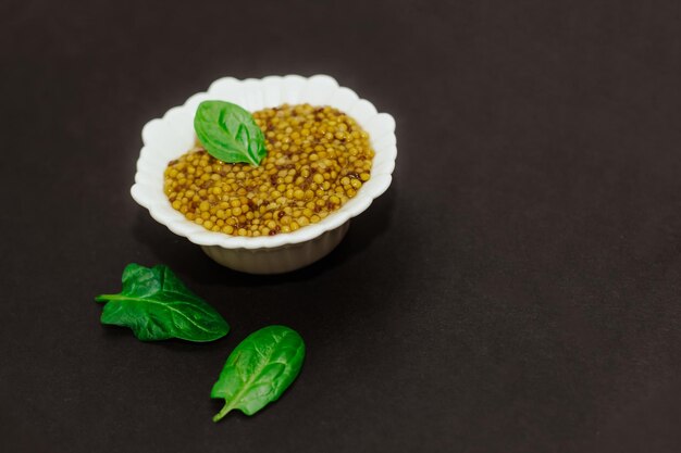 Mostaza de grano con una hoja verde en un recipiente blanco sobre un fondo negro