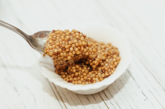 Mostaza de grano en un recipiente blanco sobre una mesa blanca