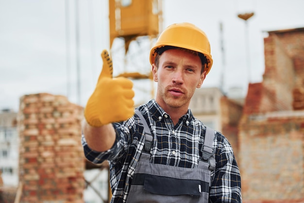 Mostra o polegar para cima Trabalhador da construção civil em uniforme e equipamento de segurança tem emprego na construção