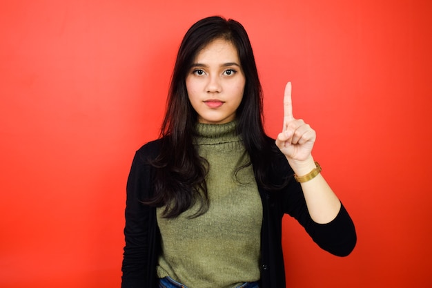 Mostrando un dedo de jóvenes hermosas mujeres asiáticas con suéter negro con fondo rojo aislado