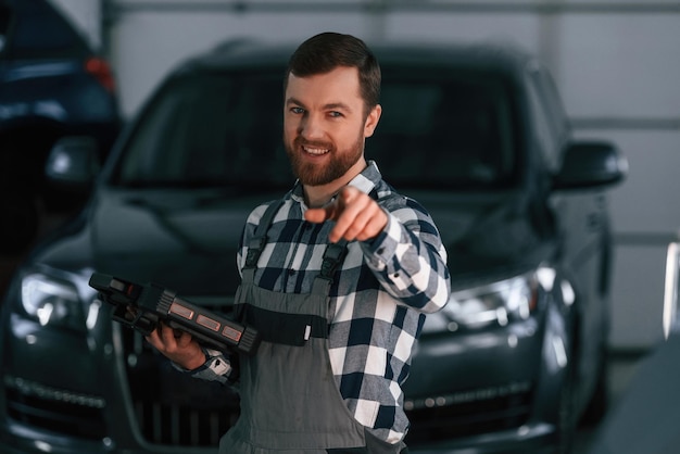 Mostrando gesto y sonriendo Sosteniendo la tableta El hombre en uniforme está trabajando en el salón del automóvil