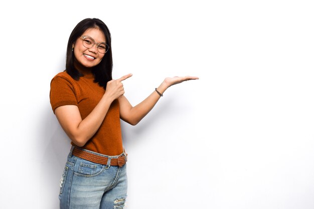 Mostrando o señalando el producto en la palma Jóvenes hermosas mujeres asiáticas visten camisa naranja aislada en blanco