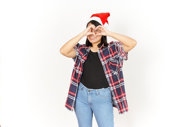 Mostrando o sinal do coração de uma bela mulher asiática vestindo uma camisa xadrez vermelha e um chapéu de Papai Noel isolado no branco