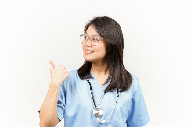 Mostrando y señalando el producto con el pulgar del joven médico asiático aislado sobre fondo blanco.