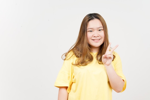 mostrando el signo de la paz de una hermosa mujer asiática con camiseta amarilla aislada de fondo blanco