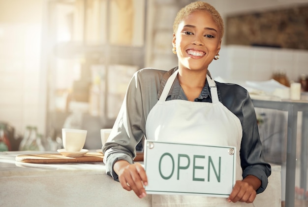 Mostrando una sonrisa y un retrato del propietario de un negocio con un cartel abierto en un café por la mañana Restaurante feliz y una mujer con una tabla en una cafetería con una sonrisa de bienvenida y un servidor en una cafetería