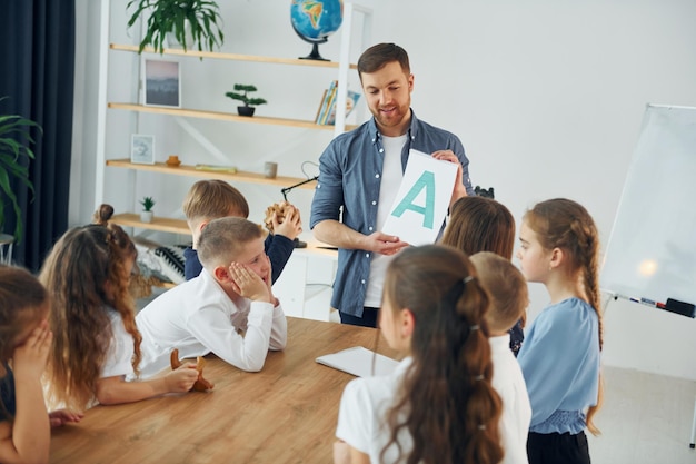 Mostrando uma carta Grupo de crianças estudantes em sala de aula na escola com professor