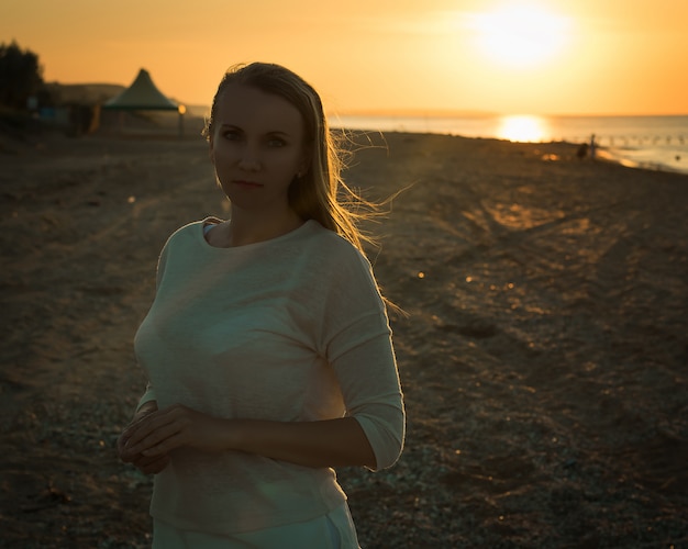 Mostre em silhueta o retrato de uma mulher em um vestido branco na praia da noite.