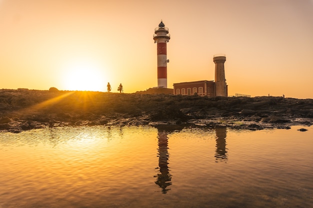 Mostre em silhueta um casal no pôr do sol no farol de Toston, Punta Ballena, perto da cidade de El Cotillo, Ilha de Fuerteventura, Ilhas Canárias. Espanha