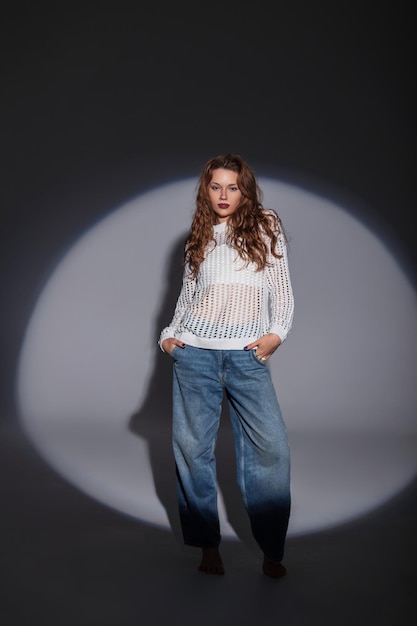 Foto mota bela garota elegante em uma blusa branca elegante com jeans da cidade no estúdio em um fundo escuro com luz circular