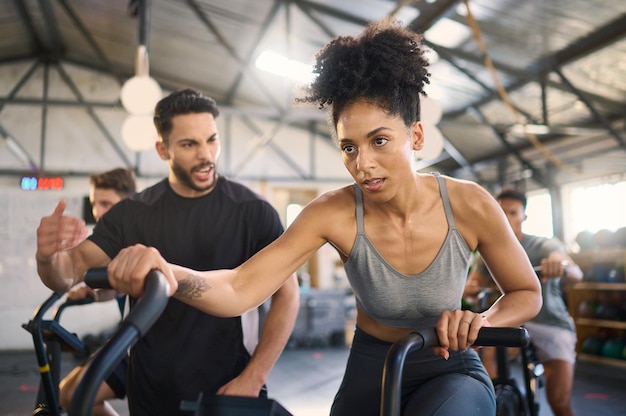 Foto motivación de la bicicleta estática y entrenador personal con una mujer negra en el gimnasio para hacer ejercicio o estar en forma entrenamiento de bienestar y ciclismo con una mujer y un entrenador trabajando juntos en un club de salud o bienestar