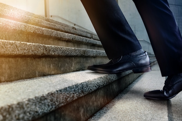 Foto motivación y desafiante concepto de carrera. pasos hacia adelante en un éxito. sección baja del empresario walking up en escalera. hombre en vestido formal negro