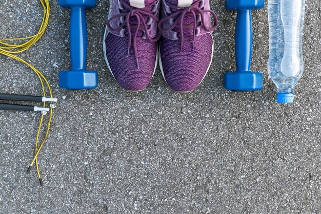 Motivado para treinar. Duas lixeiras azuis e uma corda de pular estão perto de calçados esportivos roxos. Garrafa de água deitada nas proximidades. Fitness como hobby