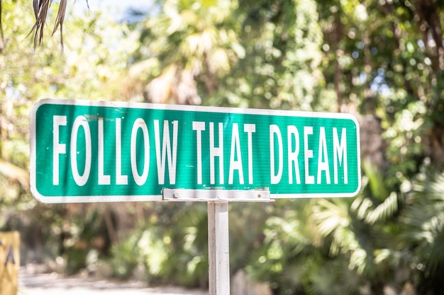 Motivationszitat mit der aufschrift follow that dream auf einem schild neben einer straße in der natur