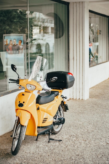 Moto amarilla con un baúl negro se encuentra cerca de una vitrina en la calle