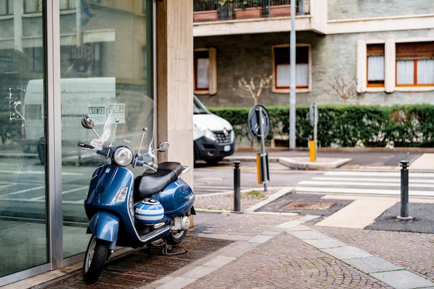 Moto azul con un casco a rayas está estacionado sobre adoquines cerca de una vitrina de vidrio