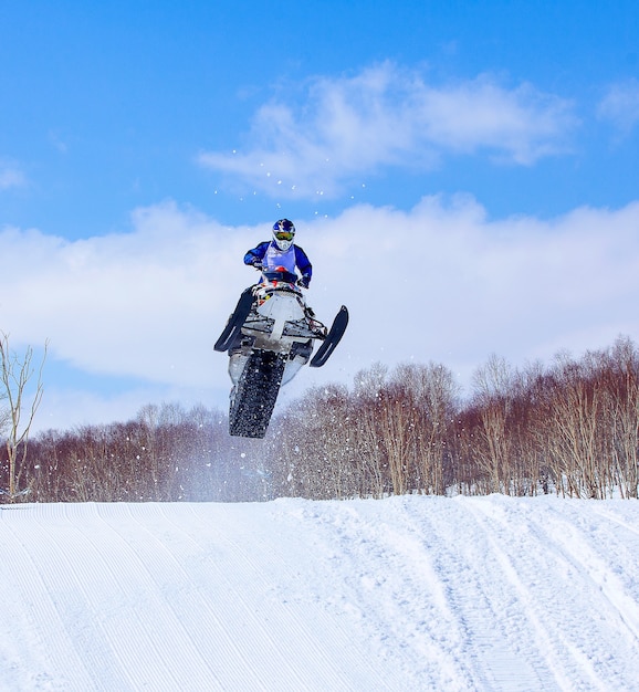 Moto de nieve en salto de altura por encima de la pista.