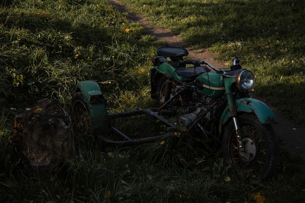 Moto verde velha abandonada com um carrinho na grama