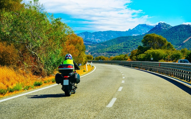 Motocicleta en carretera en Costa Smeralda en la isla de Cerdeña en Italia en verano. Motociclista conduciendo scooter en la autopista de Europa. Hombre en ciclomotor en la autopista. provincia de Olbiai. Técnica mixta.