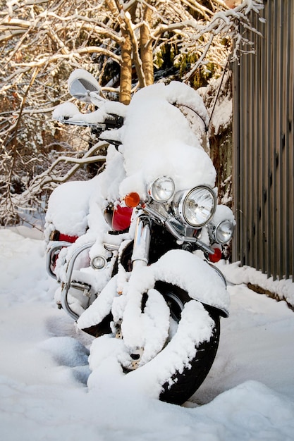 Motocicleta bajo la nieve en el patio de la casa.