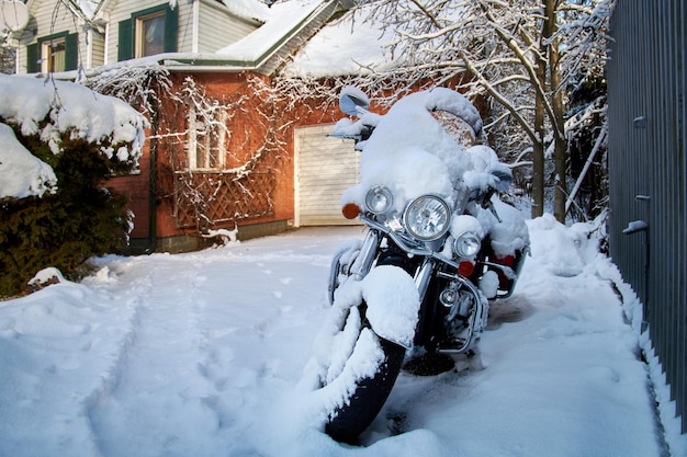 Motocicleta bajo la nieve en el patio de la casa.