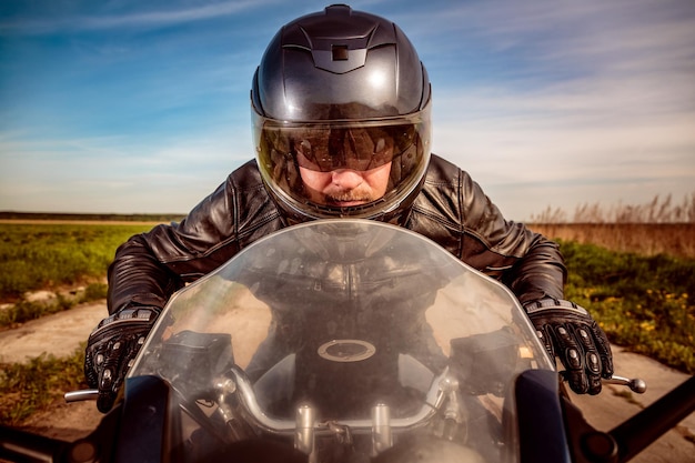 Motociclista con casco y chaqueta de cuero corriendo en la carretera