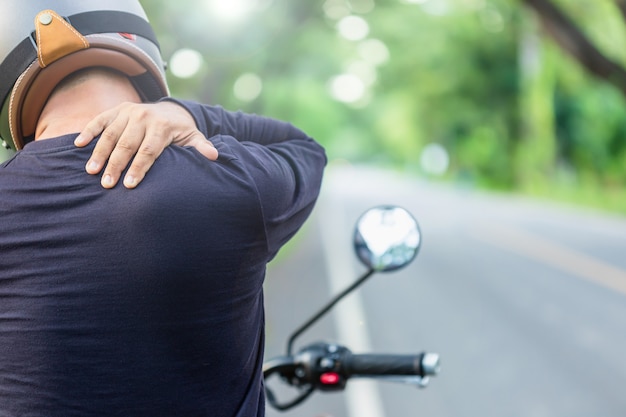 Motociclista com dor ou conceito cansado: piloto homem tocando em seu pescoço ou ombro e se sentindo cansado após um longo passeio de moto Filmagem ao ar livre na estrada com espaço de cópia