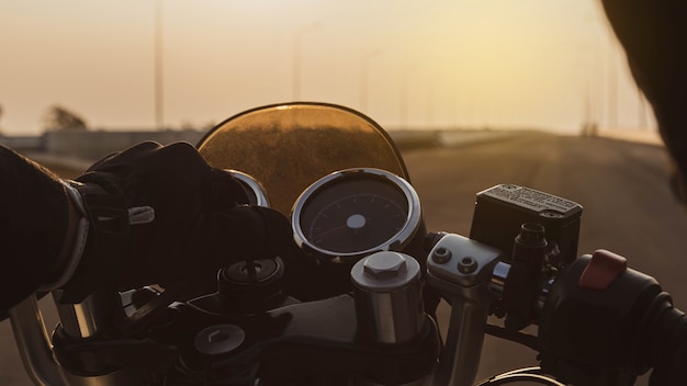 Motociclista começando a motocicleta em uma estrada de asfalto na rodovia ao pôr do sol, detalhes da barra de direção.