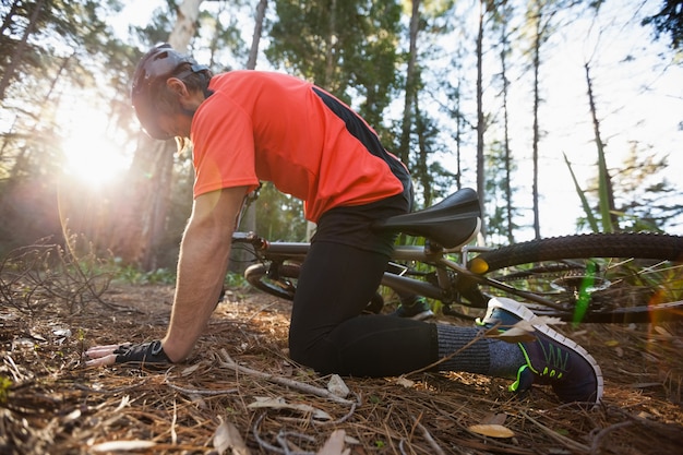 Motociclista de montanha masculino caído de sua bicicleta na floresta