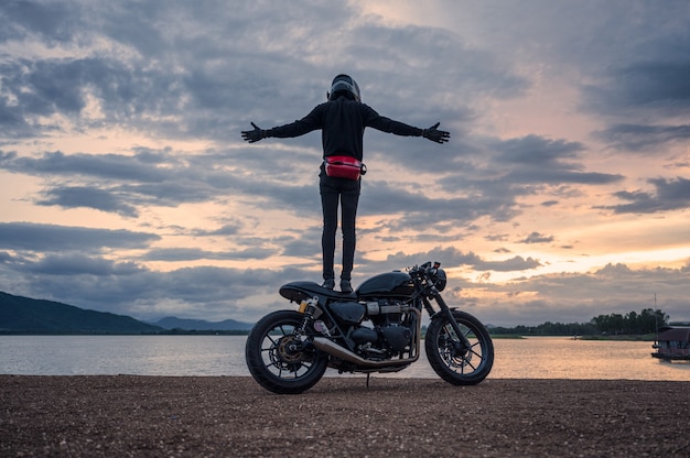 Motociclista em pé na bicicleta grande vintage com céu no reservatório