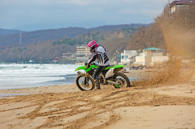 Motociclista em um traje de proteção anda de moto no mar, salpicos voam debaixo das rodas.