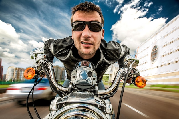 Motociclista engraçado em óculos de sol e corrida de jaqueta de couro na estrada (lente olho de peixe)