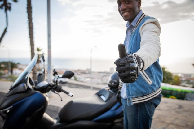 Un motociclista feliz muestra el pulgar hacia arriba mientras está de pie junto a su concepto de seguridad vial scooter