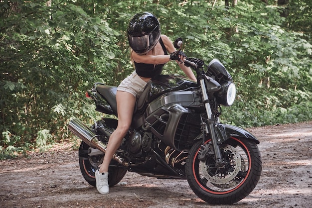 Motociclista jovem em um capacete dirige uma motocicleta em uma estrada florestal viaja sozinha