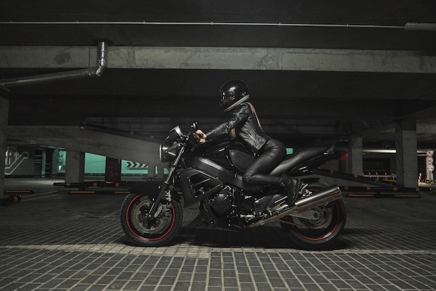 Motociclista jovem em um capacete sentado em uma motocicleta na garagem subterrânea