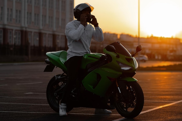 Motociclista masculino elegante irreconhecível no capacete sentado na moto estacionada na cidade