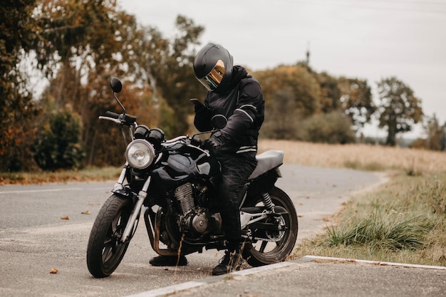 Motociclista masculino em uma jaqueta quente e capacete em clima frio de outono na estrada com uma motocicleta c